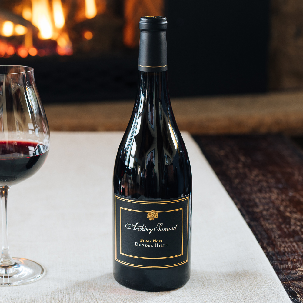 Dundee Hills Pinot Noir bottle on table with fireplace in background