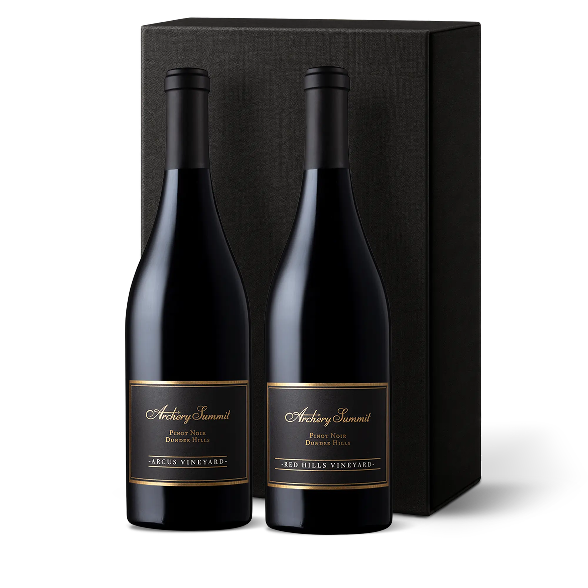 Two dark wine bottles with gold and black labels stand in front of a tall black gift box. The labels read Archery Summit and indicate Pinot Noir from Arcus Vineyard and Red Hills Vineyard.